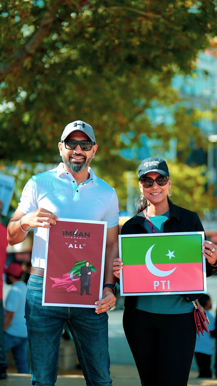 Smiling man and woman standing outside and holding a flag of pakistan and a sign